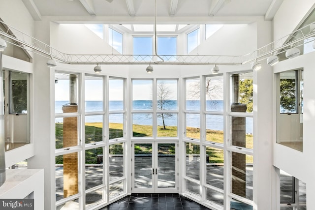 unfurnished sunroom with plenty of natural light, a water view, and a view of the beach