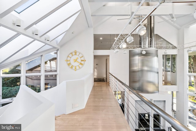 corridor with beamed ceiling, a skylight, high vaulted ceiling, and light hardwood / wood-style flooring