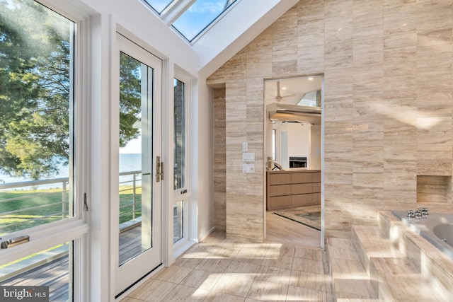 doorway to outside with lofted ceiling with skylight, tile patterned flooring, a water view, and tile walls