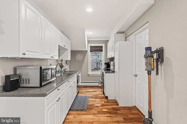 kitchen with sink, electric range, a baseboard radiator, light hardwood / wood-style floors, and white cabinetry