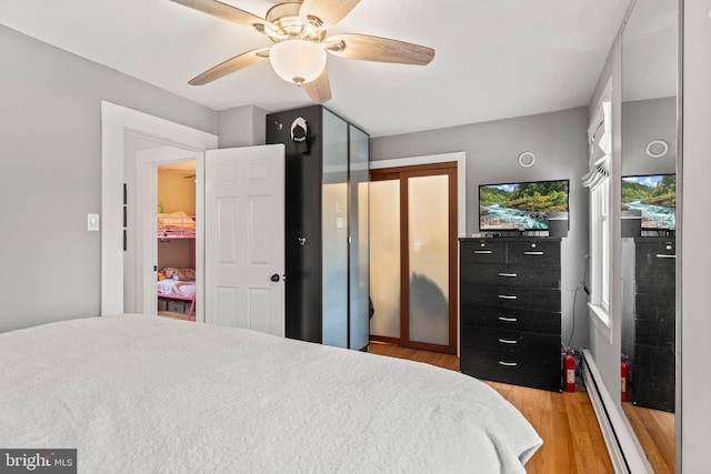 bedroom with ceiling fan, baseboard heating, and light hardwood / wood-style flooring