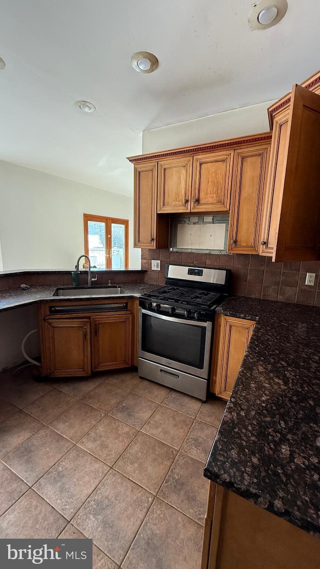 kitchen featuring sink, stainless steel gas range, dark stone countertops, tile patterned floors, and decorative backsplash