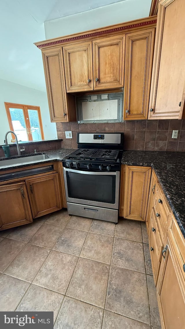 kitchen featuring vaulted ceiling, gas stove, dark stone counters, decorative backsplash, and sink