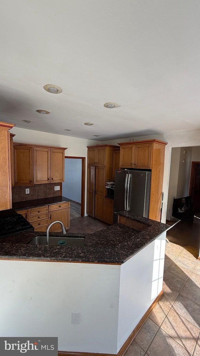 kitchen featuring sink, dark stone countertops, light tile patterned floors, kitchen peninsula, and stainless steel refrigerator