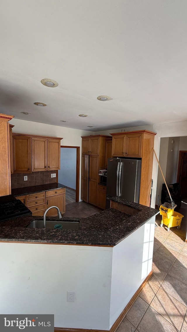 kitchen with sink, light tile patterned floors, kitchen peninsula, stainless steel refrigerator, and backsplash