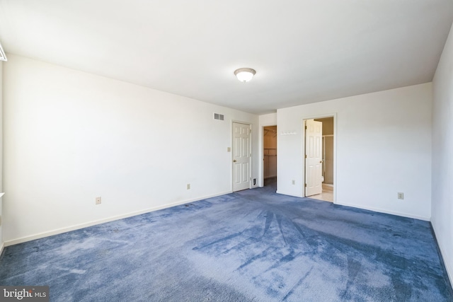 unfurnished bedroom with dark colored carpet and a walk in closet