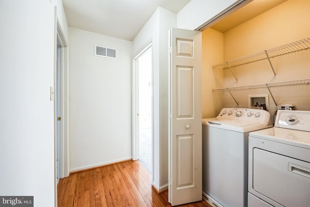 clothes washing area with washing machine and clothes dryer and light hardwood / wood-style floors