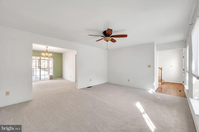 spare room featuring ceiling fan with notable chandelier and light carpet