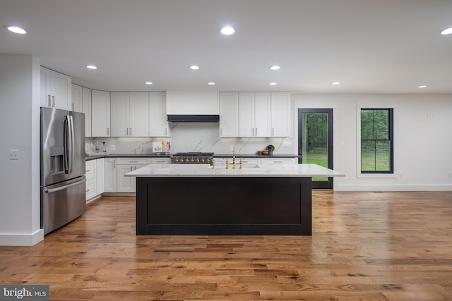 kitchen with stainless steel refrigerator with ice dispenser, tasteful backsplash, white cabinets, light hardwood / wood-style floors, and an island with sink