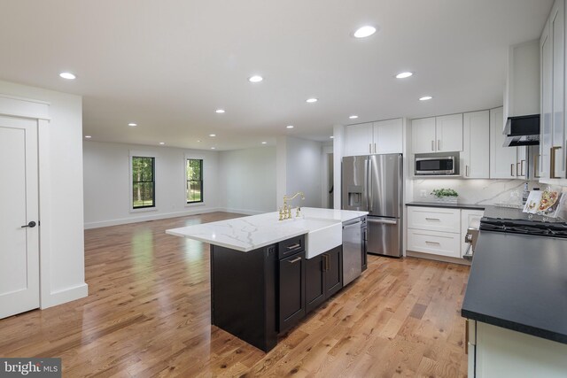 kitchen with appliances with stainless steel finishes, backsplash, a kitchen island with sink, light hardwood / wood-style flooring, and white cabinets