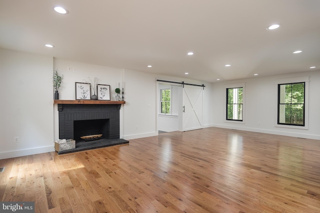 unfurnished living room featuring light hardwood / wood-style floors, a barn door, and a brick fireplace