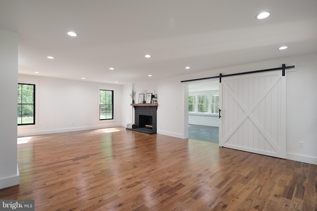 unfurnished living room featuring a barn door, hardwood / wood-style flooring, and a brick fireplace