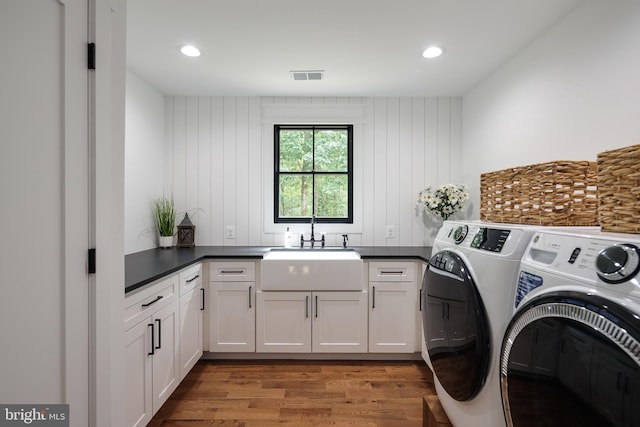 laundry room with sink, cabinets, wood walls, wood-type flooring, and washer and clothes dryer