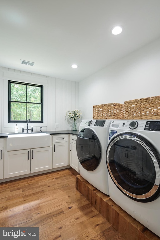 washroom with light hardwood / wood-style floors, cabinets, sink, and washing machine and dryer