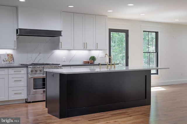 kitchen with decorative backsplash, high end stove, a kitchen island with sink, white cabinets, and light hardwood / wood-style floors