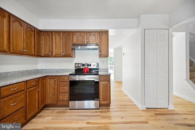 kitchen featuring light wood-type flooring, light stone counters, and stainless steel range with electric stovetop