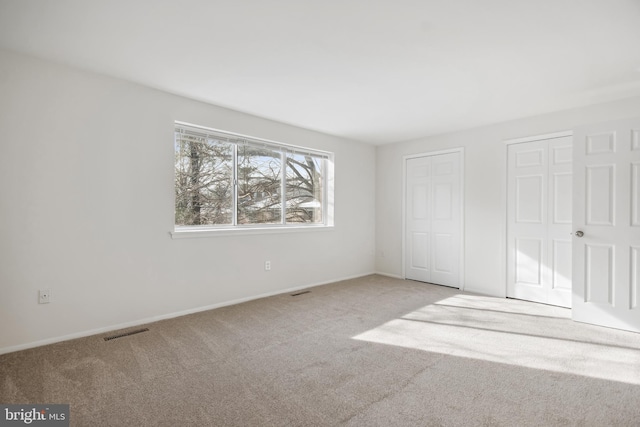 unfurnished bedroom with light colored carpet and two closets