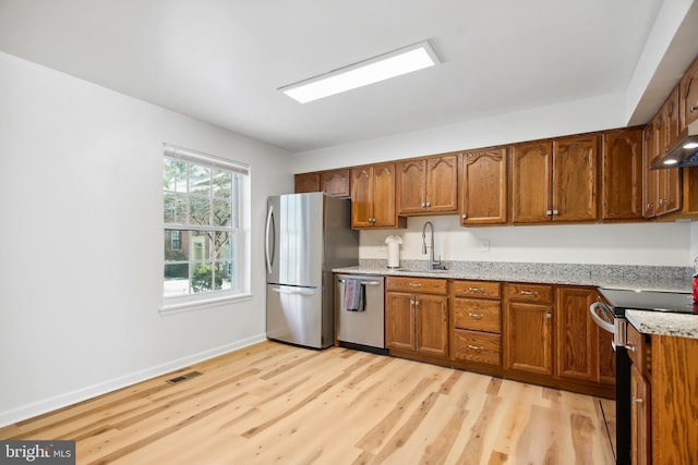 kitchen with appliances with stainless steel finishes, sink, light stone counters, and light hardwood / wood-style floors