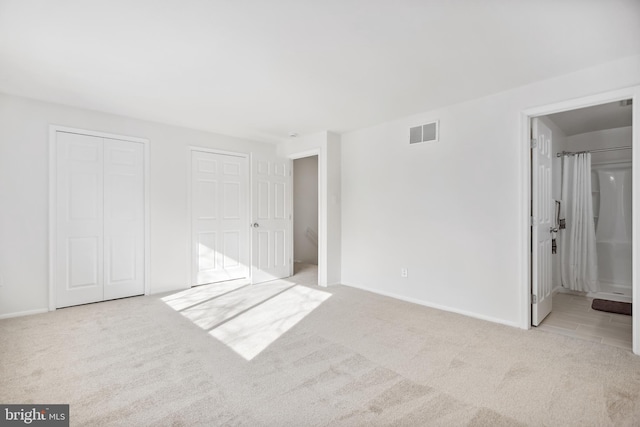 unfurnished bedroom featuring light colored carpet, multiple closets, and ensuite bathroom