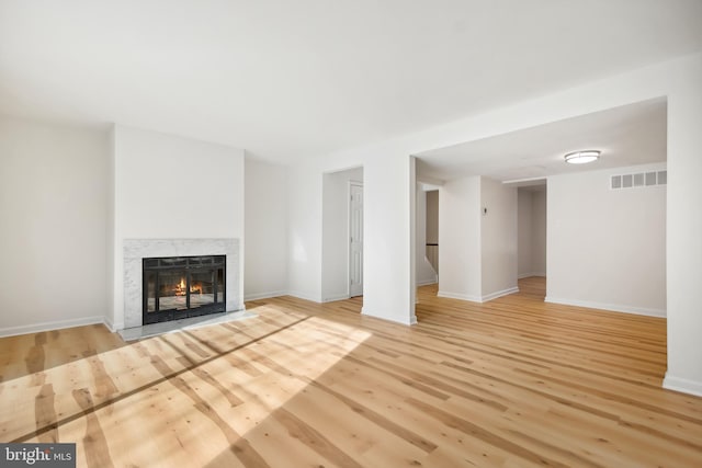 unfurnished living room featuring a premium fireplace and light hardwood / wood-style flooring