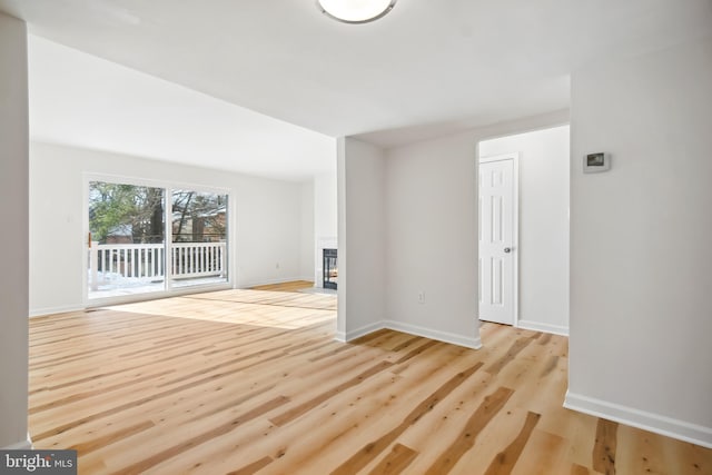 spare room featuring a tiled fireplace and light hardwood / wood-style floors