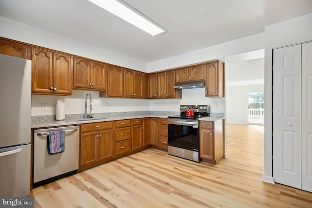 kitchen with light stone counters, sink, stainless steel appliances, and light hardwood / wood-style floors