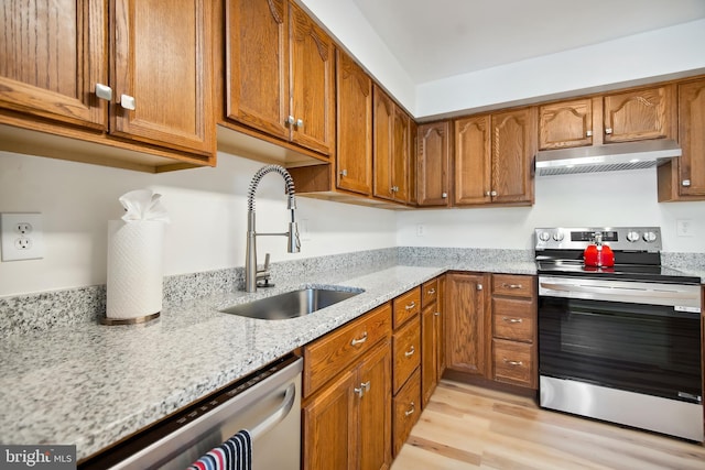 kitchen featuring appliances with stainless steel finishes, sink, light stone counters, and light hardwood / wood-style floors