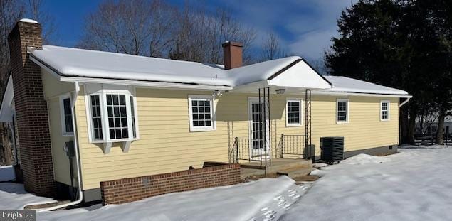 snow covered rear of property featuring central AC unit