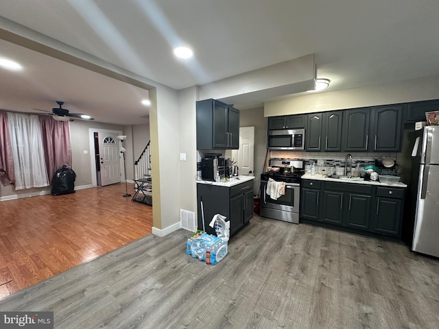 kitchen with sink, ceiling fan, decorative backsplash, light wood-type flooring, and stainless steel appliances