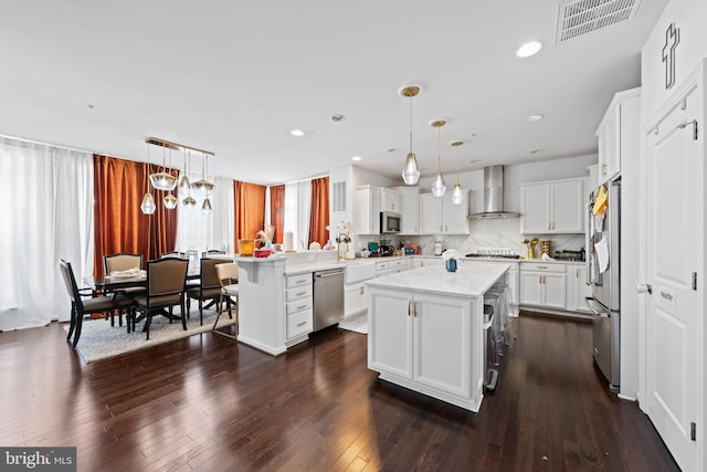 kitchen with stainless steel appliances, wall chimney range hood, pendant lighting, and a center island