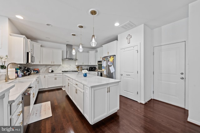 kitchen featuring white cabinets, a center island, hanging light fixtures, wall chimney range hood, and appliances with stainless steel finishes