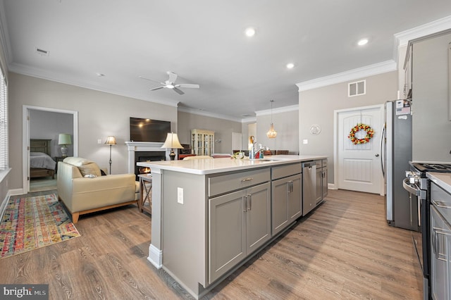 kitchen featuring appliances with stainless steel finishes, gray cabinetry, ceiling fan, a center island with sink, and crown molding