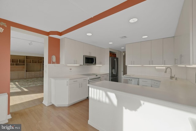 kitchen with stainless steel appliances, white cabinets, light wood-type flooring, and kitchen peninsula