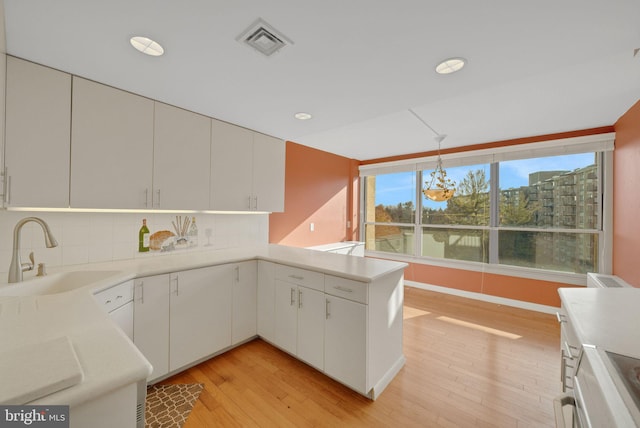 kitchen featuring pendant lighting, sink, white cabinets, backsplash, and kitchen peninsula