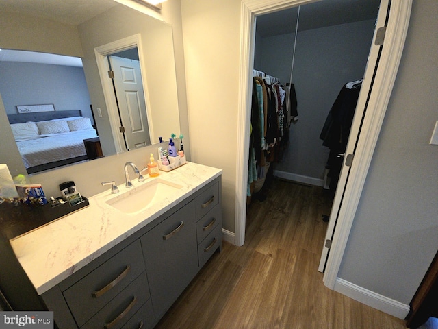 bathroom with wood finished floors, connected bathroom, vanity, baseboards, and a spacious closet