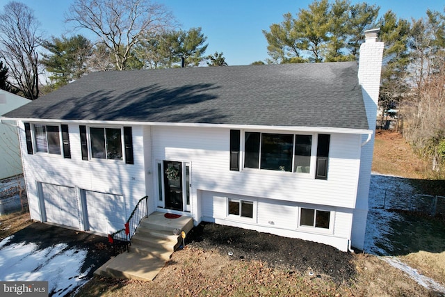 bi-level home with a garage, aphalt driveway, a chimney, and a shingled roof