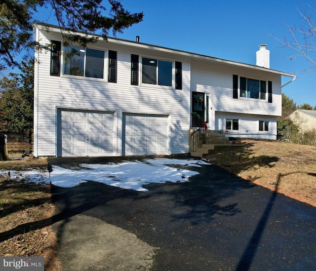 split foyer home featuring aphalt driveway, an attached garage, and a chimney