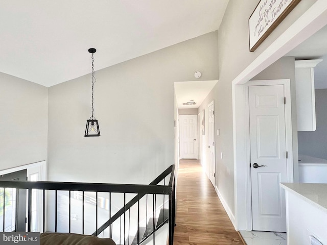 hall featuring light wood-style flooring, an upstairs landing, baseboards, and high vaulted ceiling