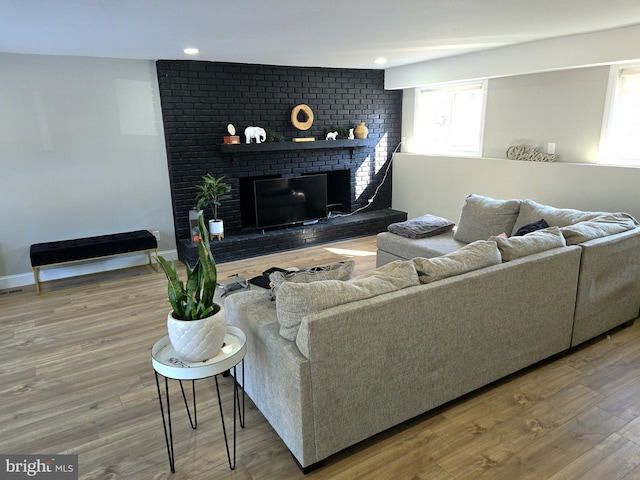 living room featuring a brick fireplace, baseboards, and wood finished floors