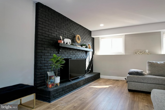 living room featuring a brick fireplace, wood finished floors, and baseboards