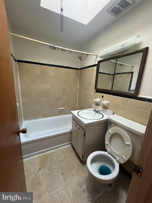 full bathroom featuring vanity, tiled shower / bath combo, toilet, and tile walls