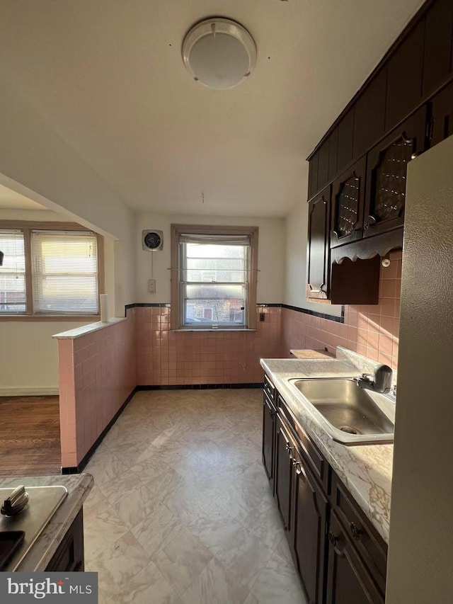 kitchen with dark brown cabinetry, tile walls, and sink