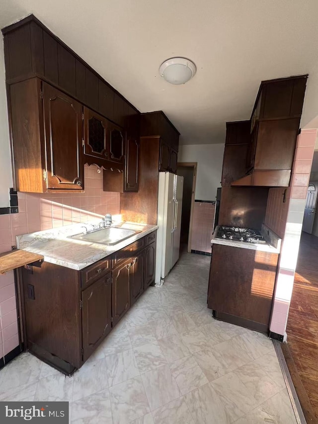 kitchen with backsplash, sink, white fridge, and dark brown cabinets