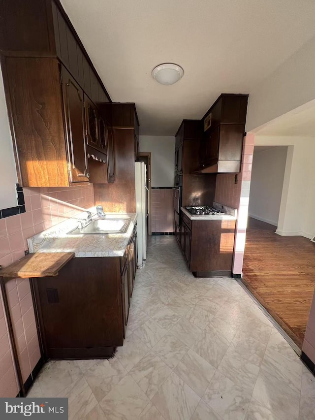 kitchen featuring stainless steel gas stovetop, sink, black oven, white fridge, and dark brown cabinetry