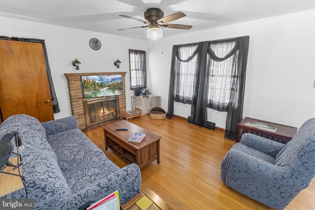 living room featuring wood-type flooring, a brick fireplace, and ceiling fan