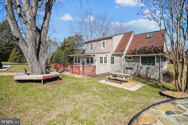 back of house featuring a shingled roof, a patio, a chimney, a deck, and a yard