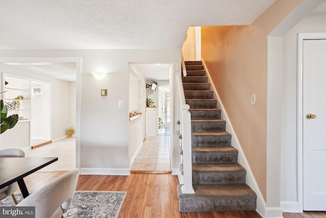 stairs with arched walkways, a textured ceiling, baseboards, and wood finished floors