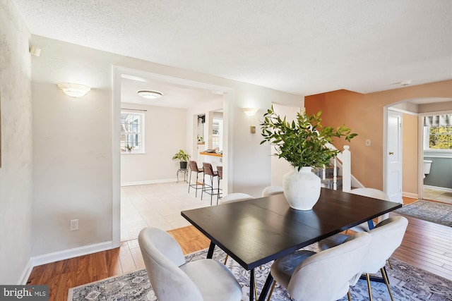 dining room with light wood-type flooring, a healthy amount of sunlight, arched walkways, and a textured ceiling