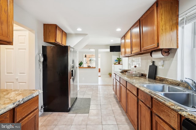 kitchen featuring brown cabinetry, light tile patterned flooring, a sink, and stainless steel refrigerator with ice dispenser