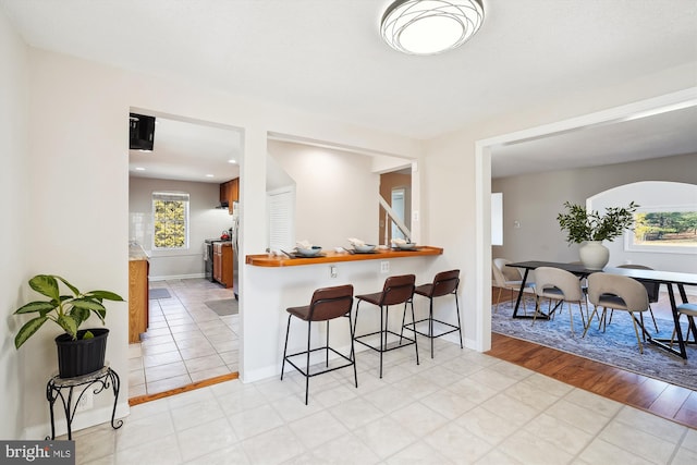 kitchen with light wood-type flooring, range with electric cooktop, baseboards, and a kitchen breakfast bar